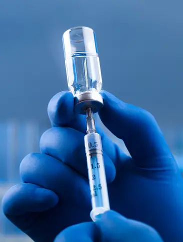 Doctor drawing vaccine from vial on a blue background